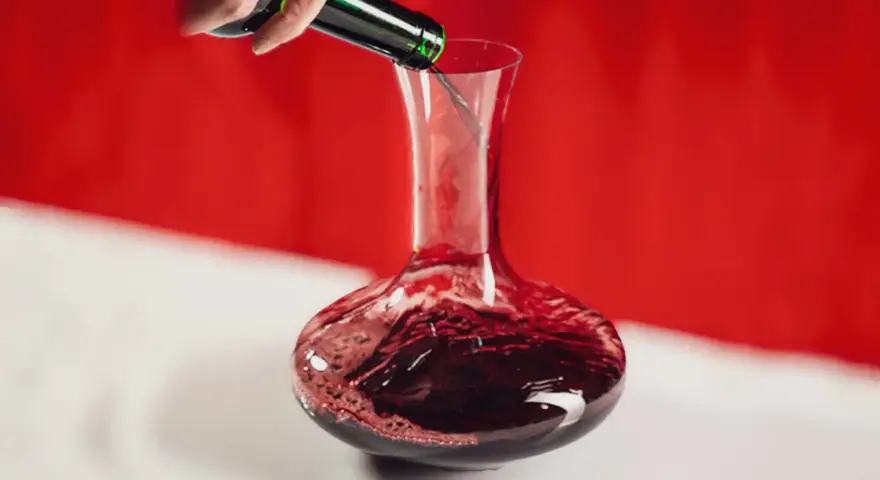 Une main verse un vin rouge profond dans une carafe. Ce pourrait être le meilleur vin du Cabardès, prêt à être savouré.