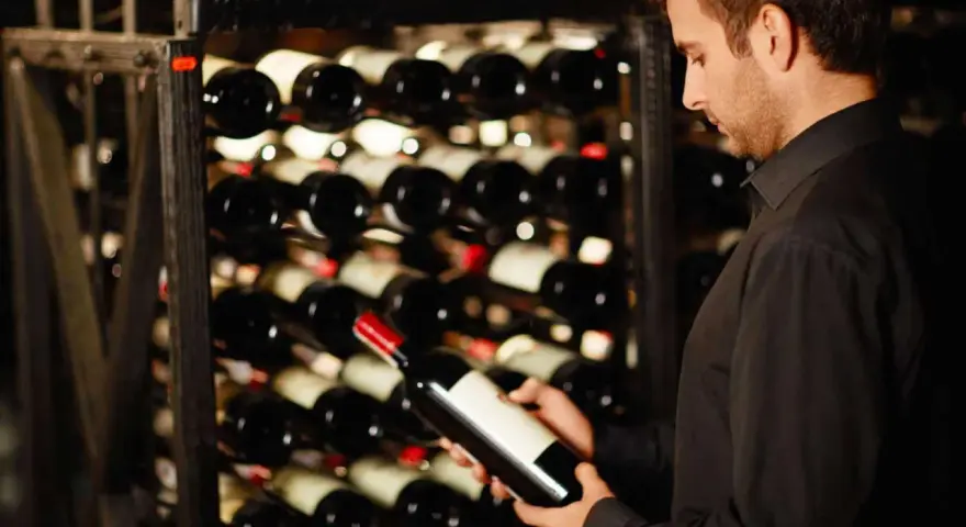 Un homme examine une bouteille de vin dans une cave. Une belle opportunité d'investir dans le vin.