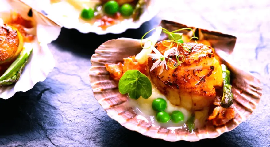 Saint-jacques poêlées, tendres et dorées, servies dans leur coquille avec des petits pois et une touche de vin rouge.