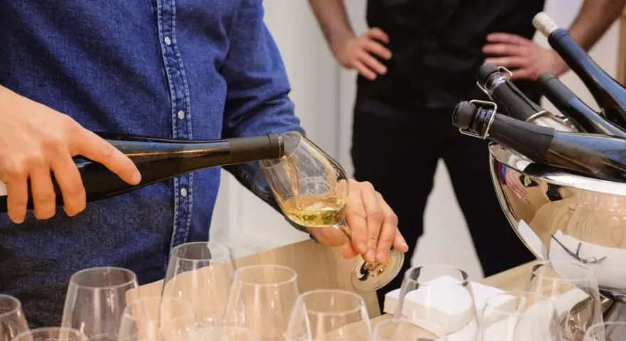 Un homme verse du vin blanc, peut-être un pinot gris, dans un verre. Il sera parfait avec du poisson.