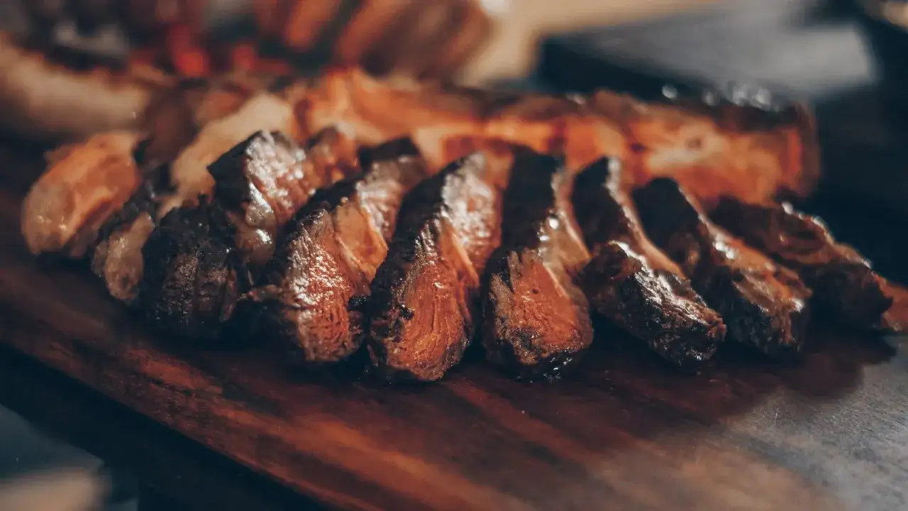 Tranches de viande grill&eacute;e sur une planche en bois. Parfait pour savoir que boire avec une pierrade viande.