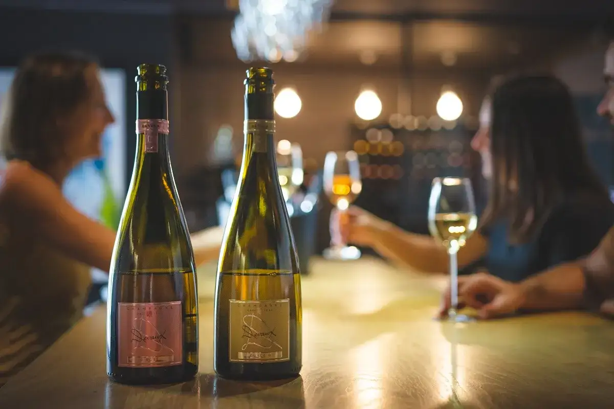 Deux bouteilles de champagne Devaux sur un bar, avec des personnes en arri&egrave;re-plan. Un avis sur le champagne Devaux ?