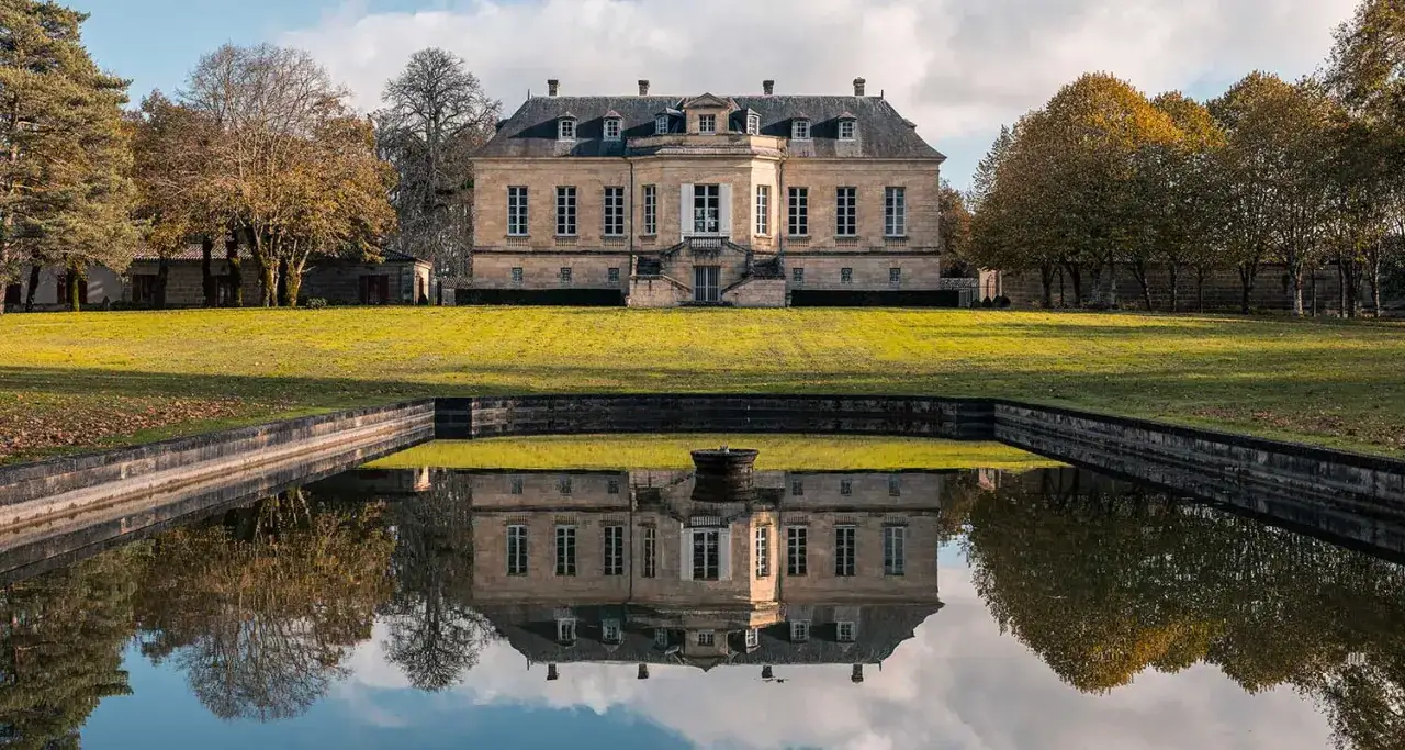 Le ch&acirc;teau La Louvi&egrave;re, majestueux et refl&eacute;t&eacute; dans un bassin, se dresse sur une pelouse verdoyante sous un ciel nuageux.