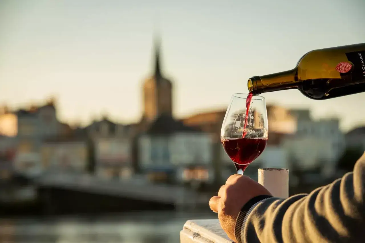 Un verre de meilleur vin rouge est servi d'une bouteille, avec une ville floue en arri&egrave;re-plan.