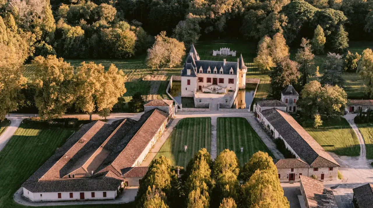Vue a&eacute;rienne du Ch&acirc;teau Olivier entour&eacute; de douves, avec ses d&eacute;pendances et ses jardins &agrave; la fran&ccedil;aise baign&eacute;s par la lumi&egrave;re dor&eacute;e du soleil couchant.