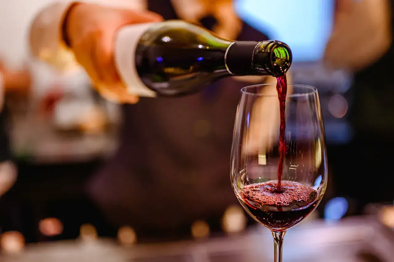 Un sommelier verse un meilleur vin rouge bordeaux dans un verre. La robe rubis intense coule, promettant une d&eacute;gustation exquise.