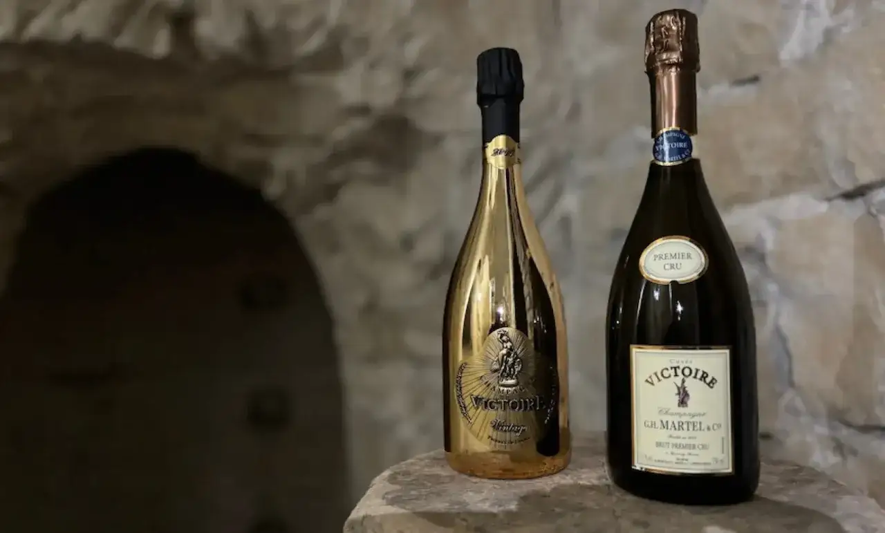 Deux bouteilles de champagne Victoire, dont une dorée, reposent sur une pierre. L'une est étiquetée 