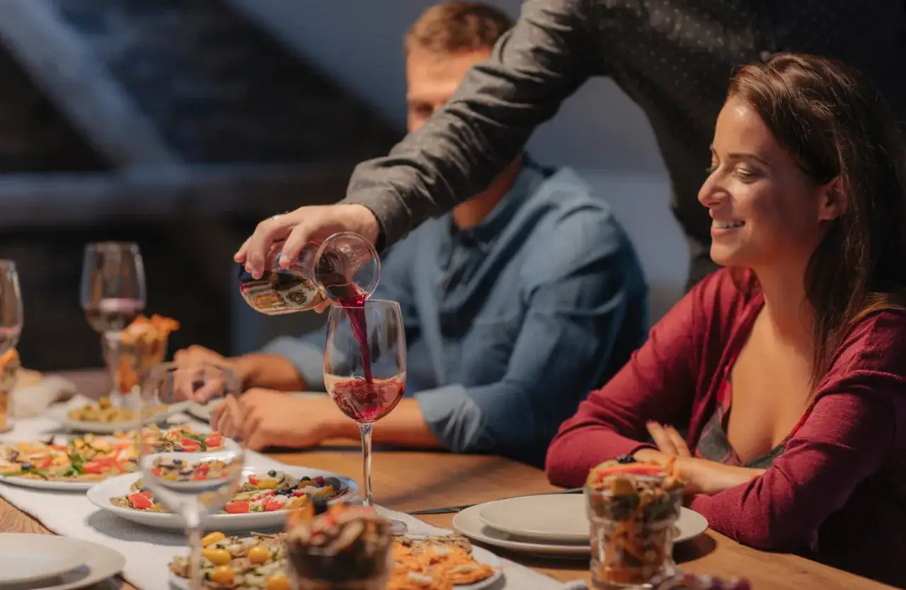 Un homme verse du vin rouge dans un verre lors d'un d&icirc;ner convivial. Le met est pr&ecirc;t &agrave; &ecirc;tre d&eacute;gust&eacute;.