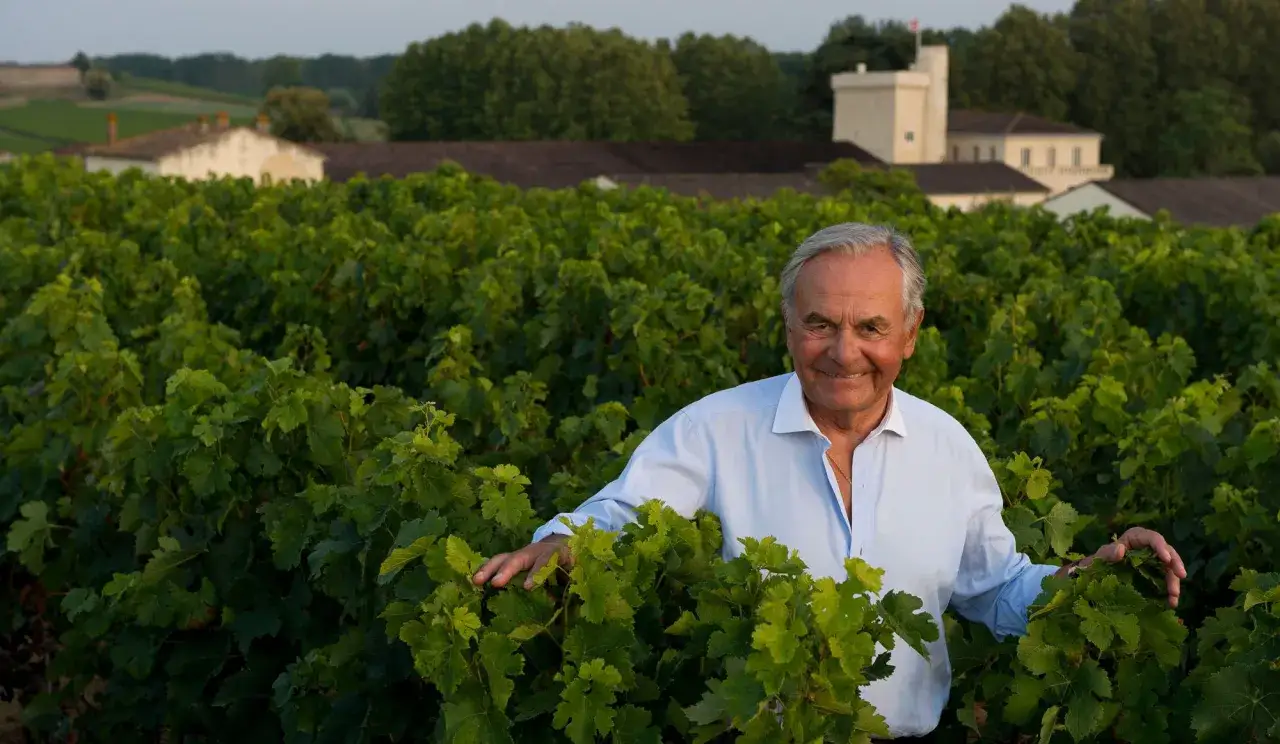 Bernard Magrez, souriant, au milieu de ses vignes verdoyantes, avec des b&acirc;timents de ch&acirc;teau en arri&egrave;re-plan.