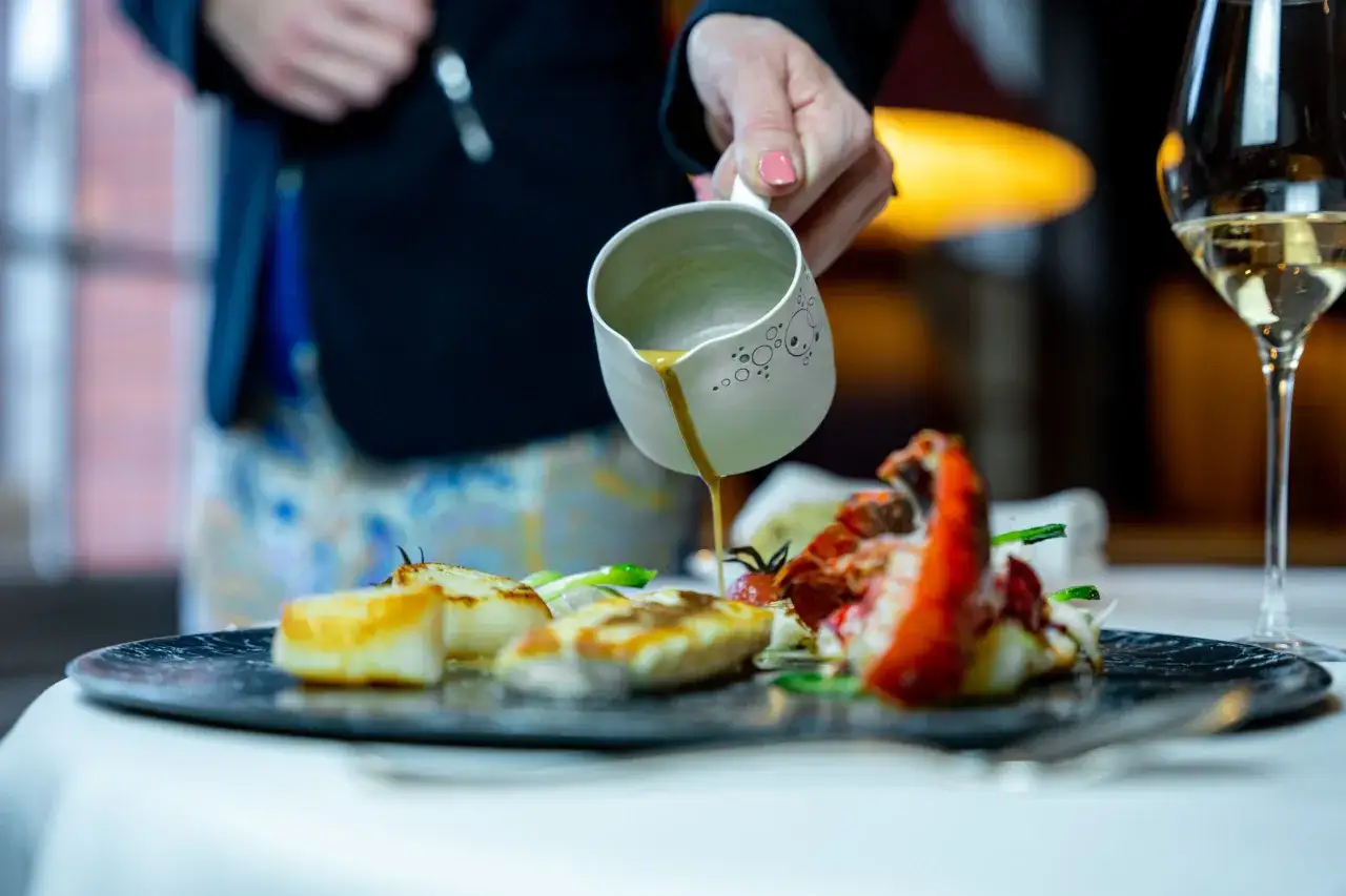 Un chef verse une sauce sur un plat de homard et de Saint-Jacques, un accord mets et vins parfait.