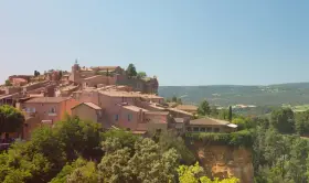 Village perché aux toits de tuiles roses, entouré de verdure. Au loin, des collines rappellent les vignes oubliées d'une Provence intemporelle.