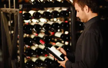 Un homme examine une bouteille de vin dans une cave. Une belle opportunité d'investir dans le vin.