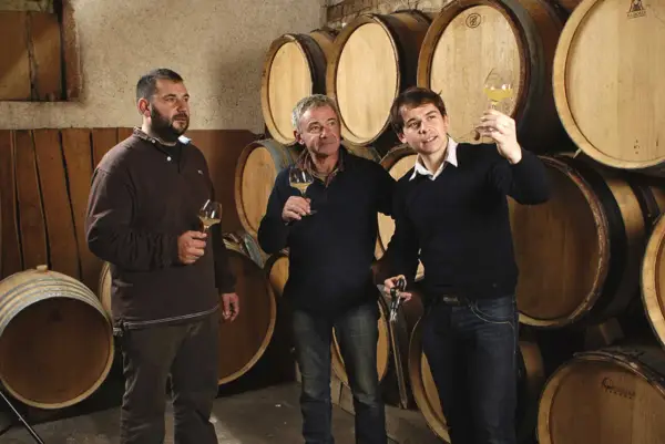 Trois hommes dégustent du vin dans la cave du domaine des Gandines, entourés de fûts de chêne.