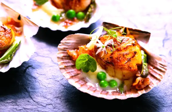 Saint-jacques poêlées, tendres et dorées, servies dans leur coquille avec des petits pois et une touche de vin rouge.