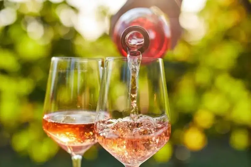 Un verre de rosé est servi dans un autre verre, sous un soleil radieux. Un moment parfait pour boire du rosé tous les jours.