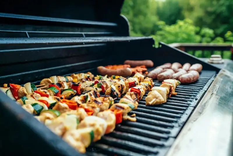 Brochettes de poulet et légumes grillés sur un barbecue, accompagnées de saucisses. Parfait pour un barbecue d'été avec un verre de vin blanc.
